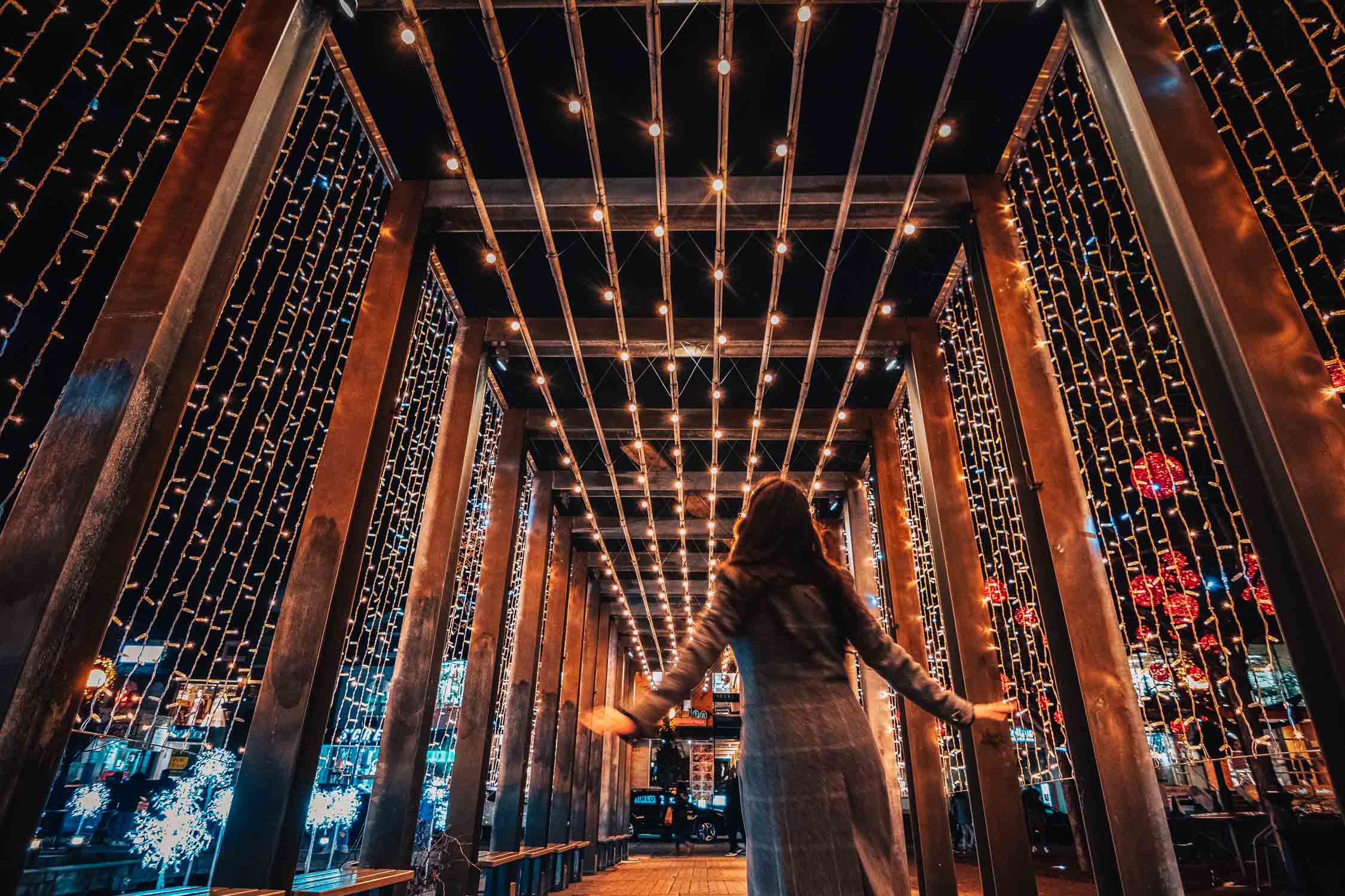 A girl walking under bridge of Christmas lights