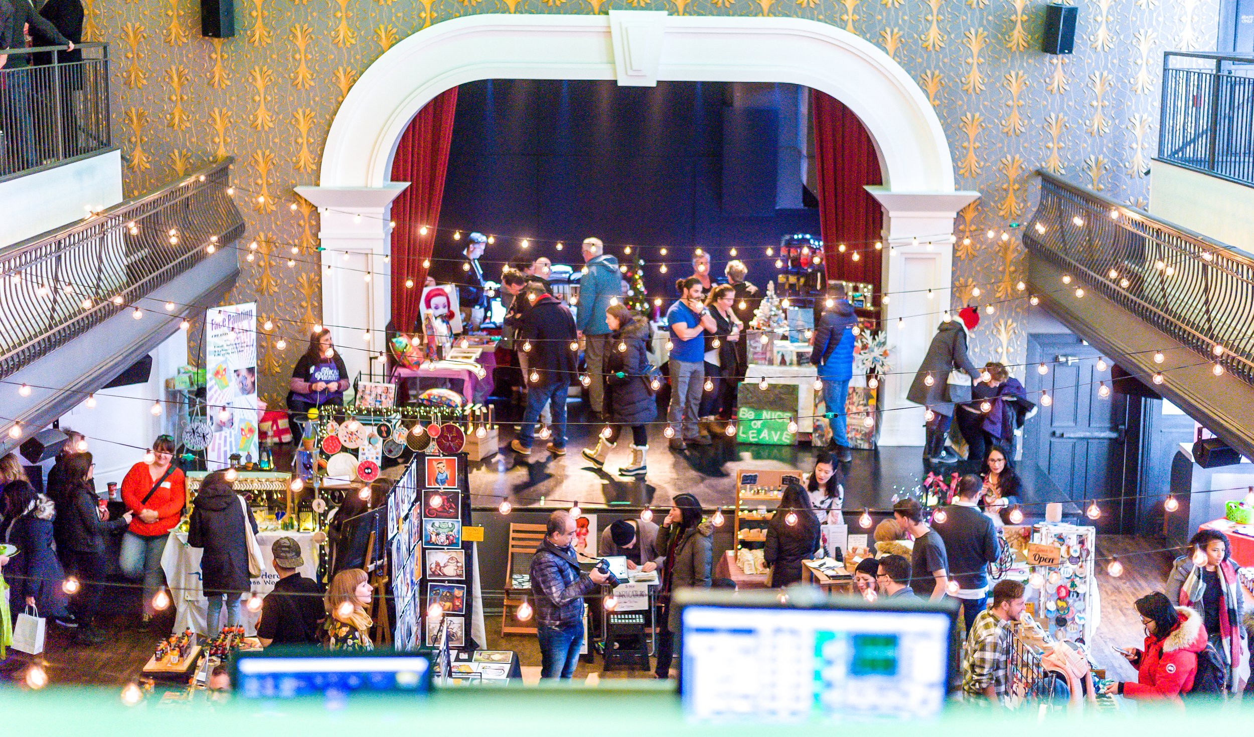 People walking around a room with Christmas lights, looking at different vendors selling things.